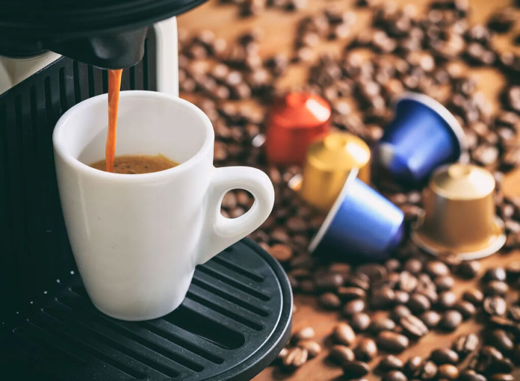 یک فنجان قهوه اسپرسو در کنار کپسول ها و دانه های قهوه